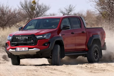A red Toyota Hilux, the best selling pickup truck, driving off-road through dusty terrain, showcasing its rugged design and robust capabilities.