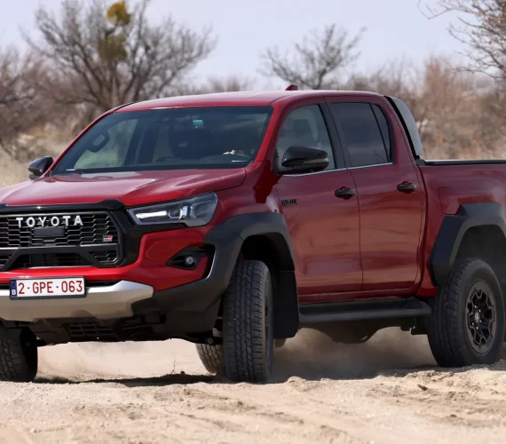A red Toyota Hilux, the best selling pickup truck, driving off-road through dusty terrain, showcasing its rugged design and robust capabilities.